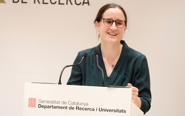Mar Reguant speaks from a lecturn with the logo of the Catalan Ministry of Research and Universities