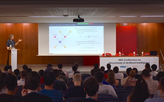 A man presenting on stage in front of a full auditorium at UAI 2024