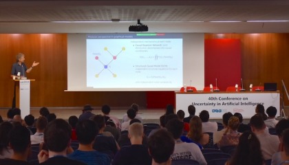 A man presenting on stage in front of a full auditorium at UAI 2024